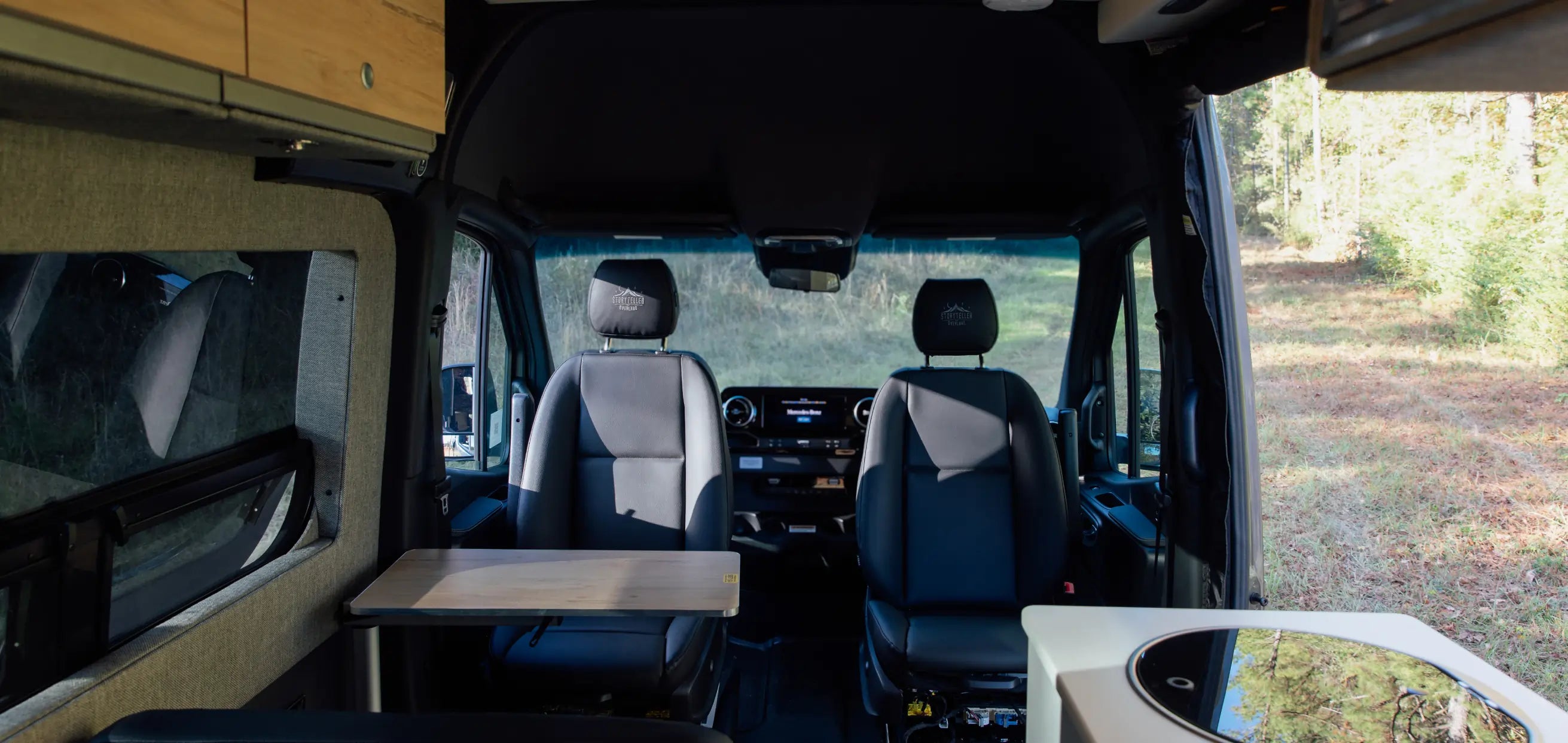 Modern adventure van interior with swivel seats, fold-out table, and compact kitchen, ideal for vanlife, campervan, overlanding, and expedition travel.