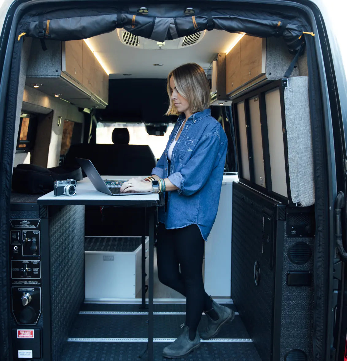 Woman working on laptop inside modern camper van conversion, adventure van interior, vanlife