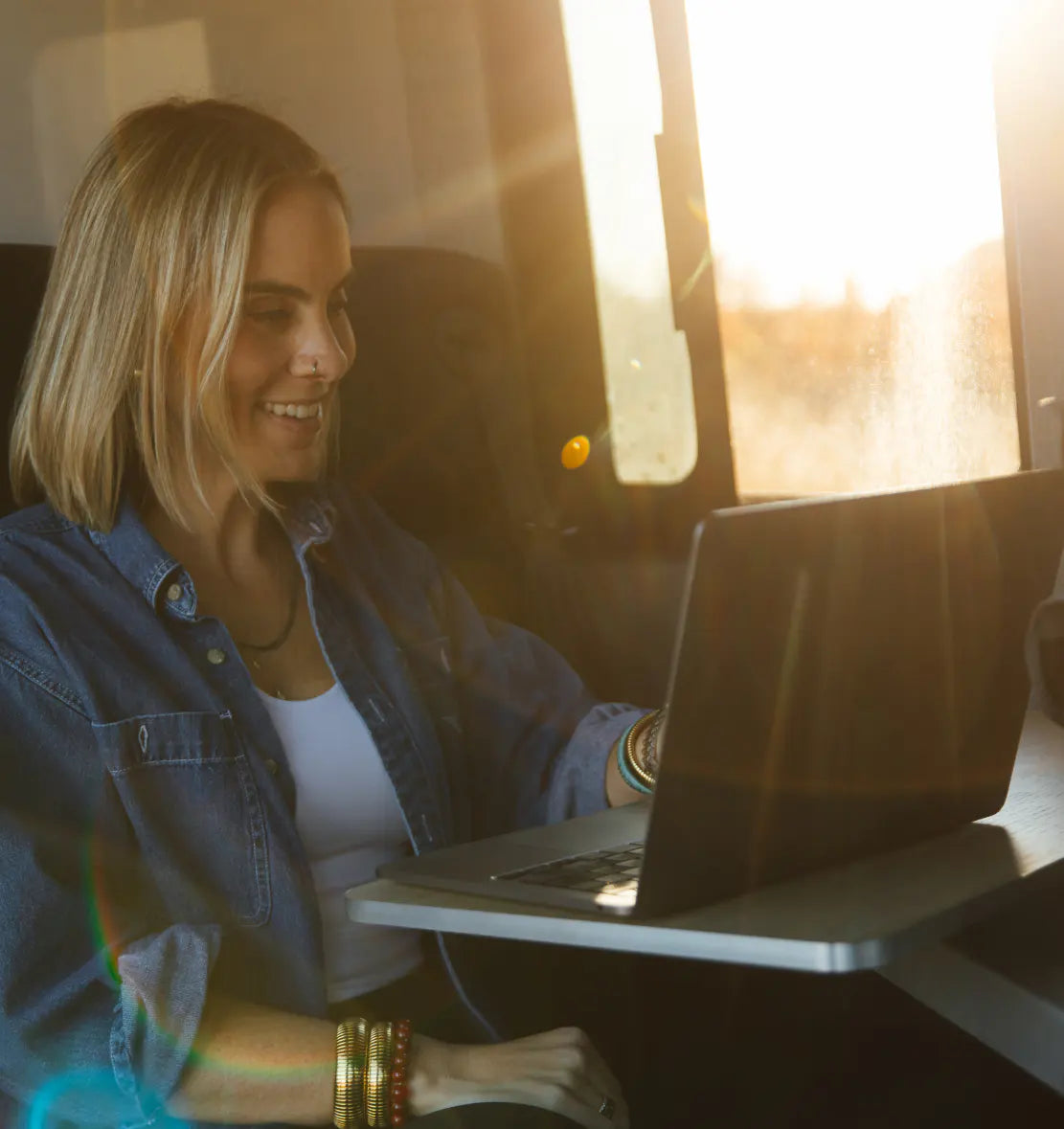Woman working on laptop inside adventure van, sunlight streaming in, campervan lifestyle