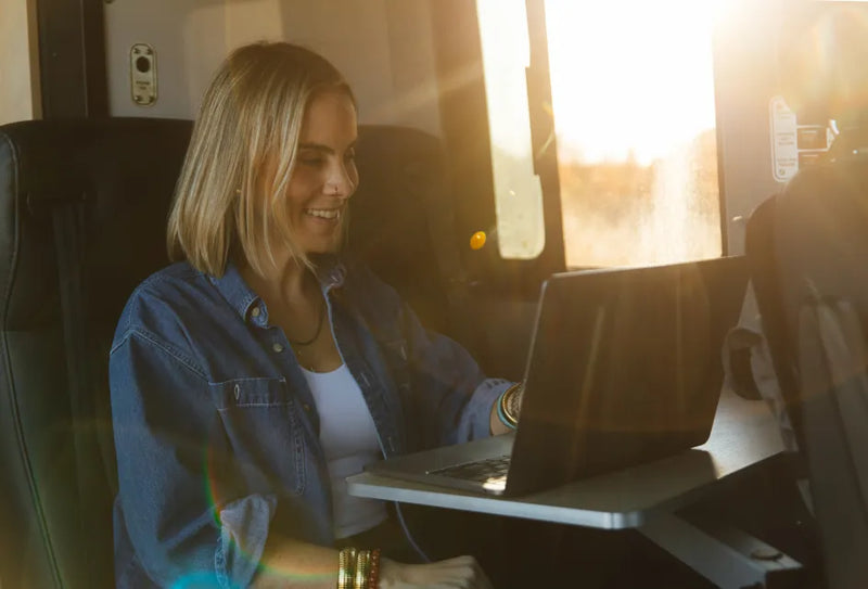 Woman working on laptop inside camper van, sunlight streaming in, adventure van lifestyle
