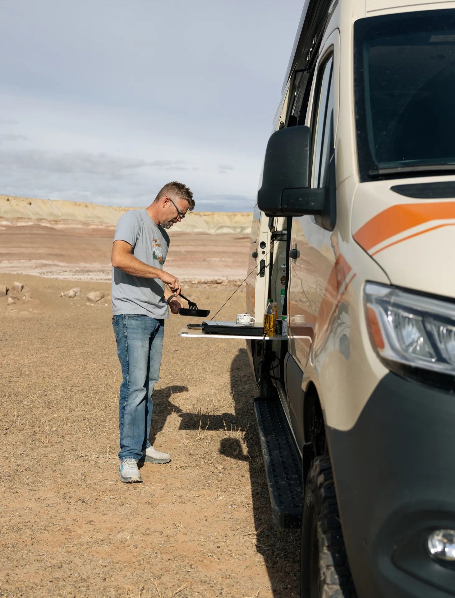Man cooking outside a Classic MODE camper van, overland adventure van in desert setting