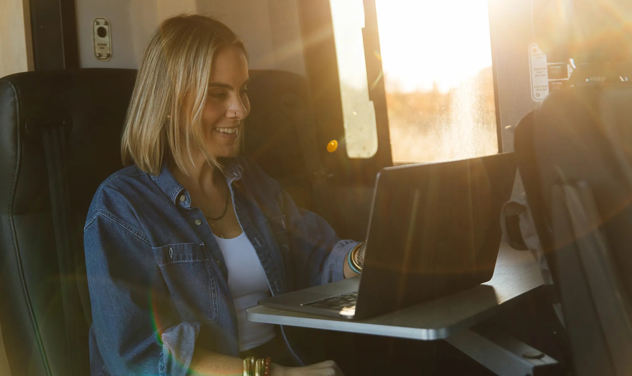 Woman working on laptop inside adventure van, enjoying vanlife and nomadic lifestyle at sunset.