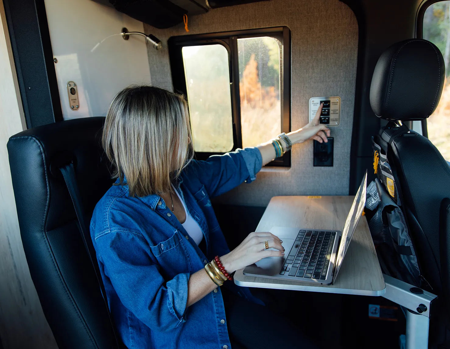 Woman working at table inside adventure van, using control panel, camper van interior