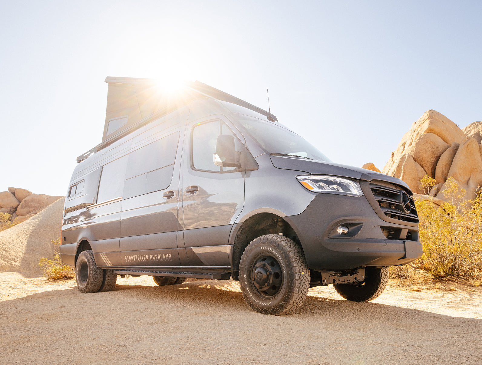 Sprinter 4x4 camper van with pop-top roof, offroad tires, in desert landscape, perfect for overlanding and adventure travel.