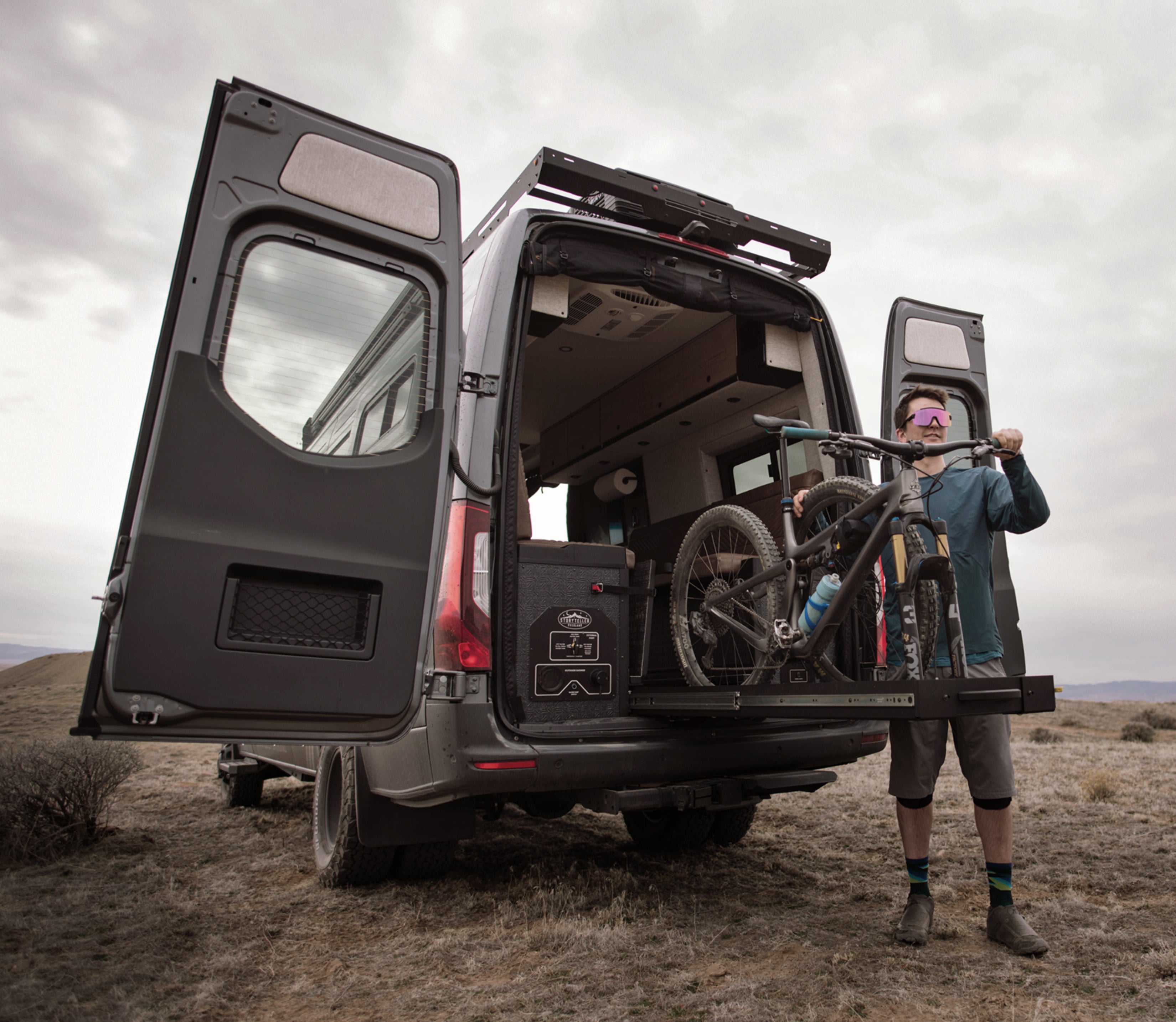 Adventure Van with rear doors open, mountain bike rack, and cyclist in offroad setting