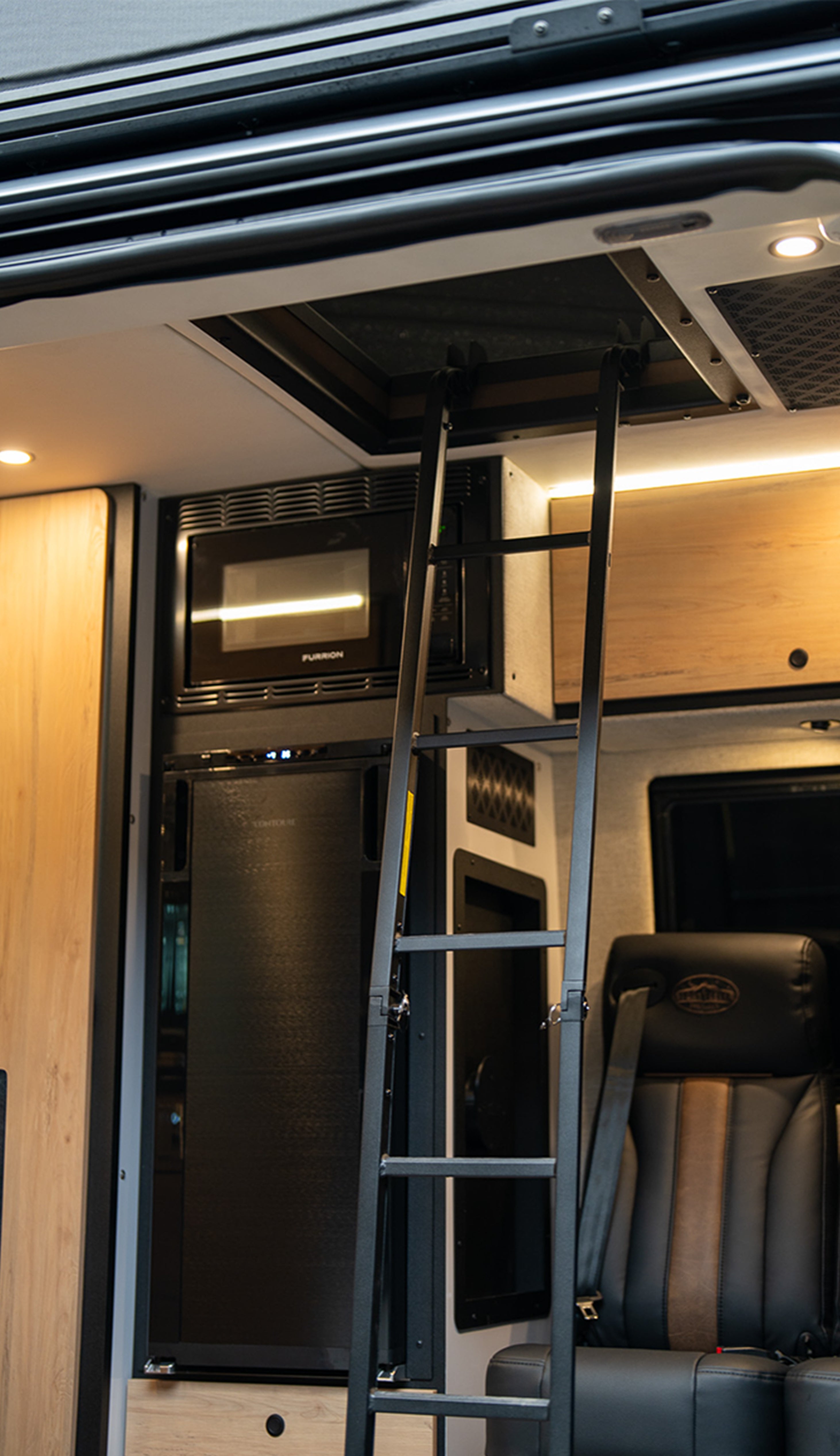 Interior of a luxury adventure van with ladder, microwave, refrigerator, and captain's chair