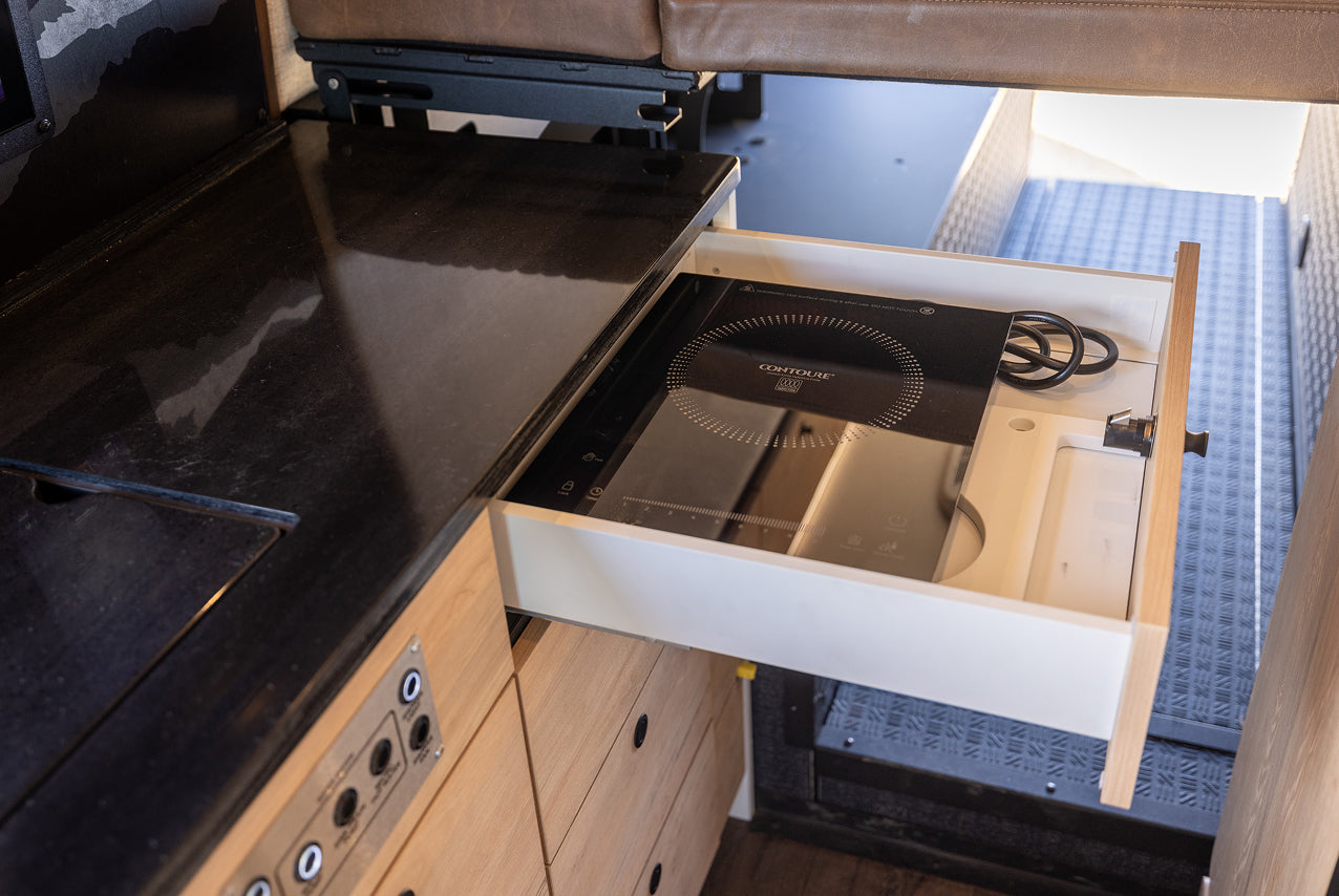 Pull-out induction stove inside adventure camper van kitchen, ideal for vanlife and overlanding.