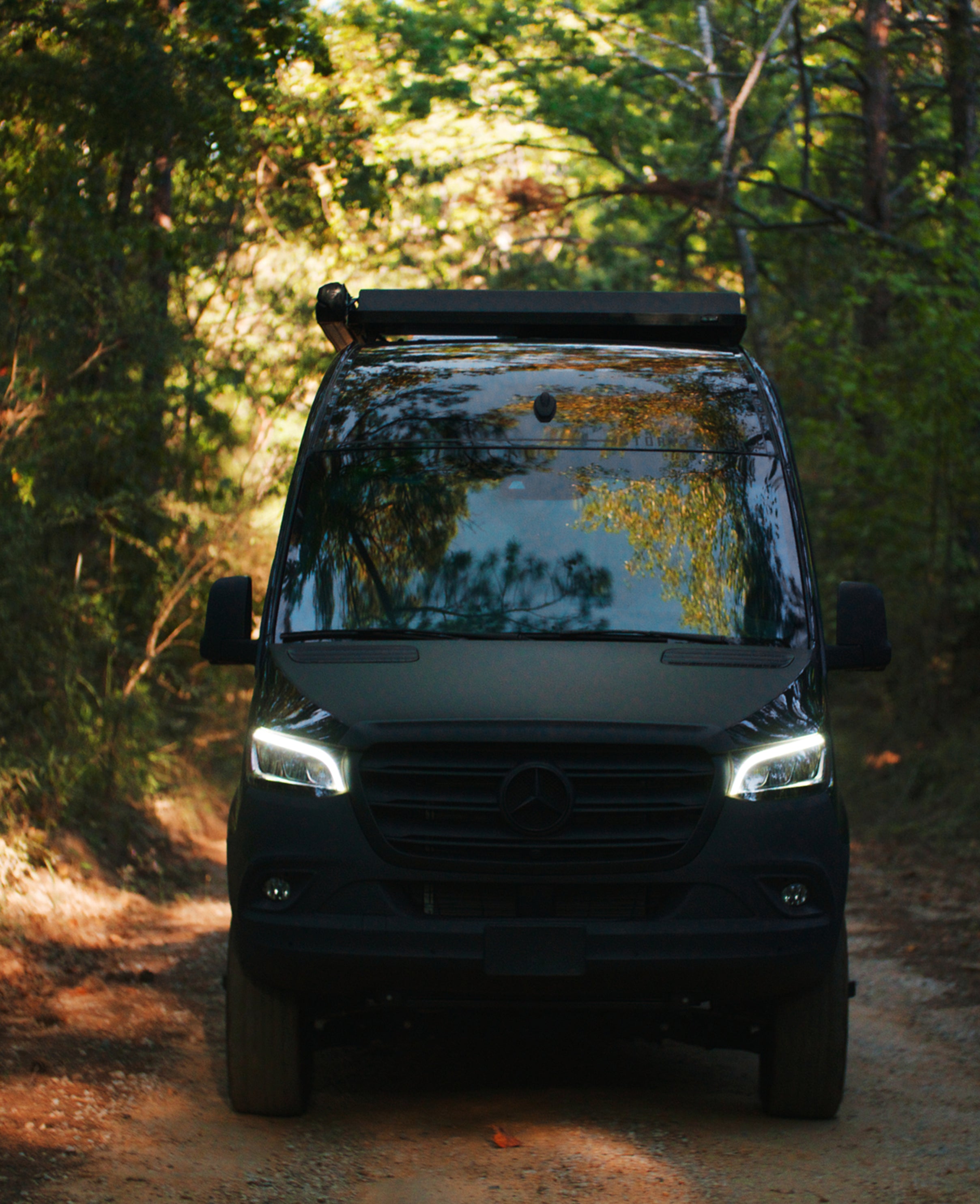 Black Sprinter 4x4 camper van on forest trail, ideal for overland, vanlife, adventure travel