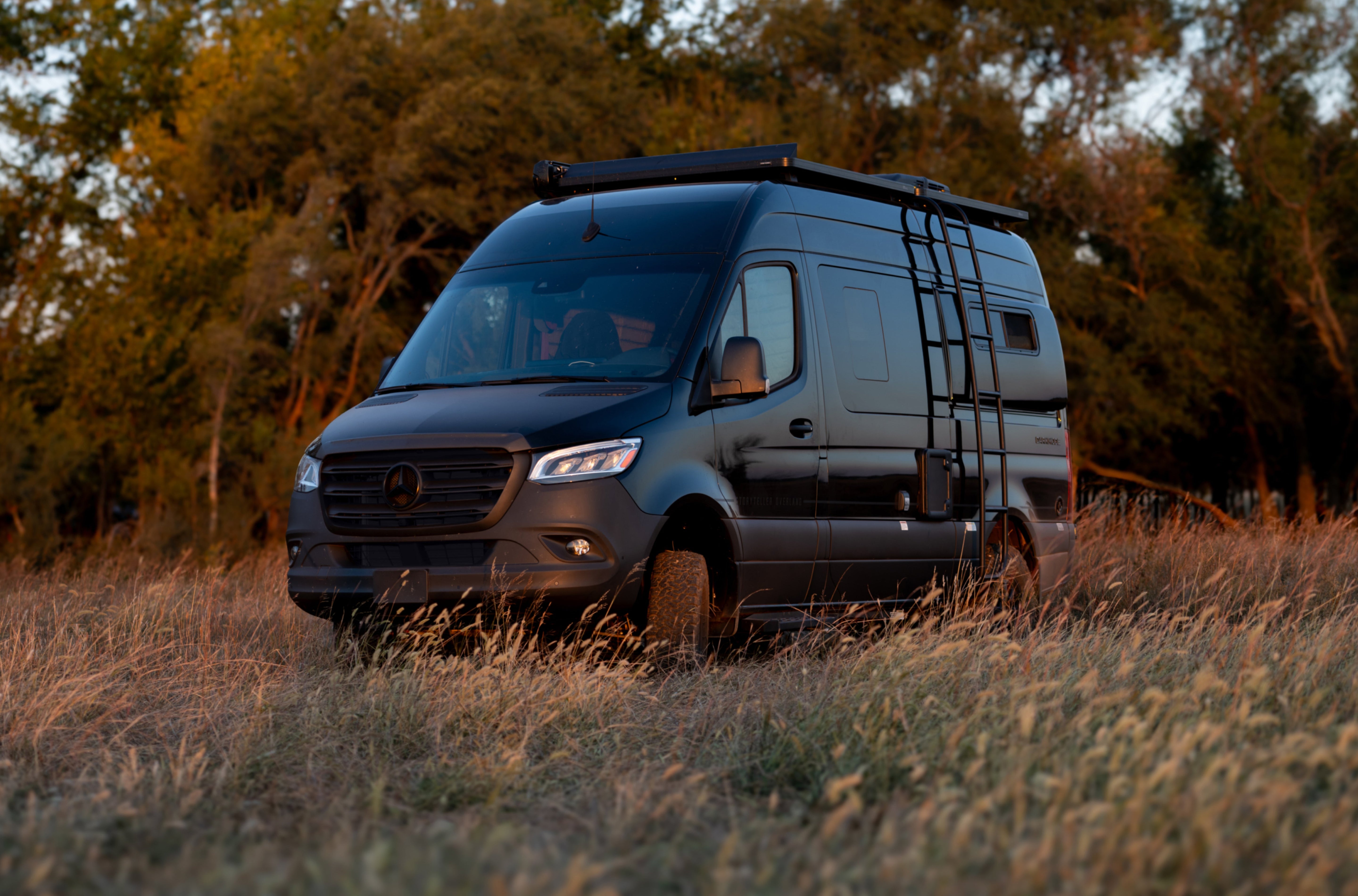Black Sprinter 4x4 camper van with ladder parked offroad, ideal for overlanding and adventure travel