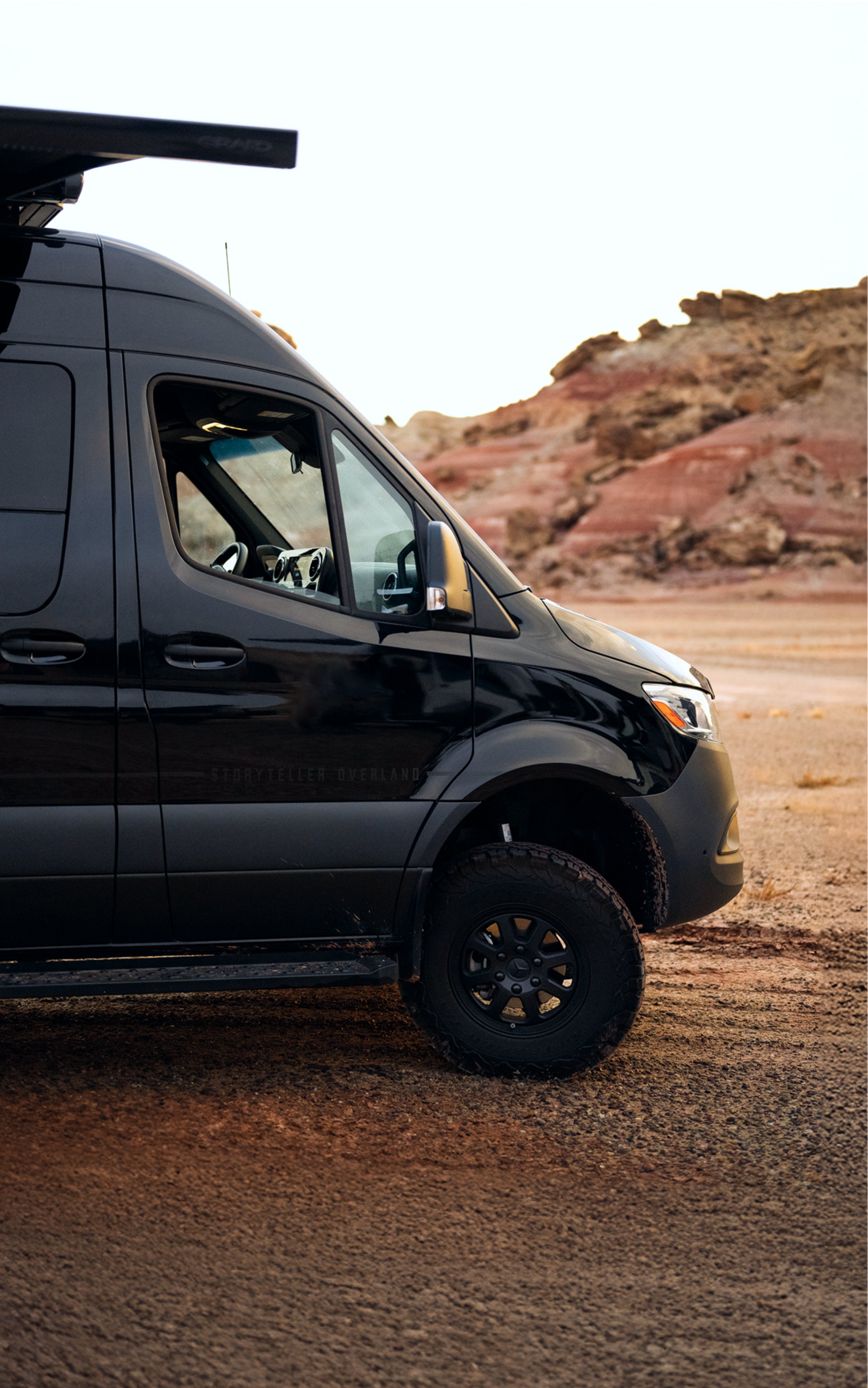 Black Sprinter 4x4 adventure van exterior side view, offroad in desert landscape
