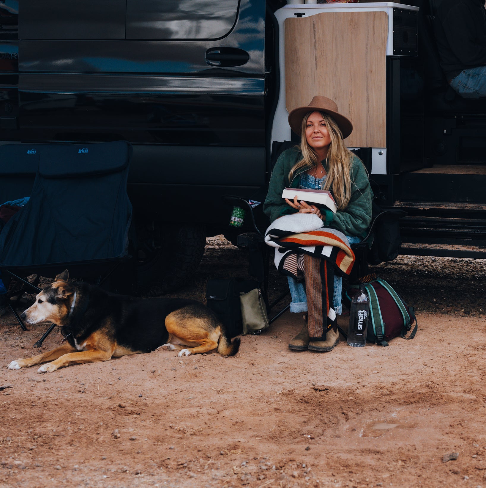 Woman and dog relaxing by overland camper van, adventure van lifestyle outdoors