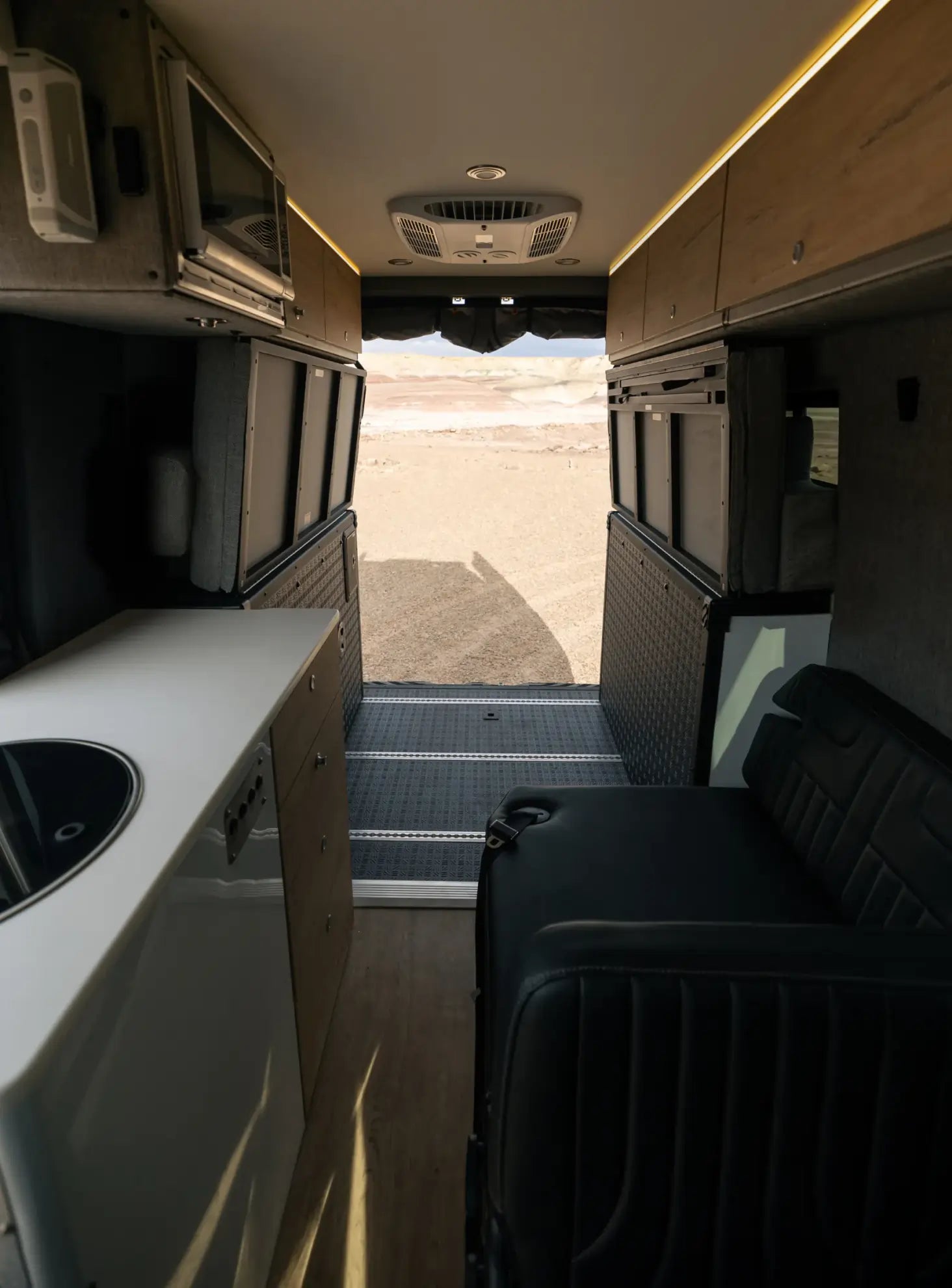 Modern adventure van interior with kitchenette, seating, and open rear doors for overlanding