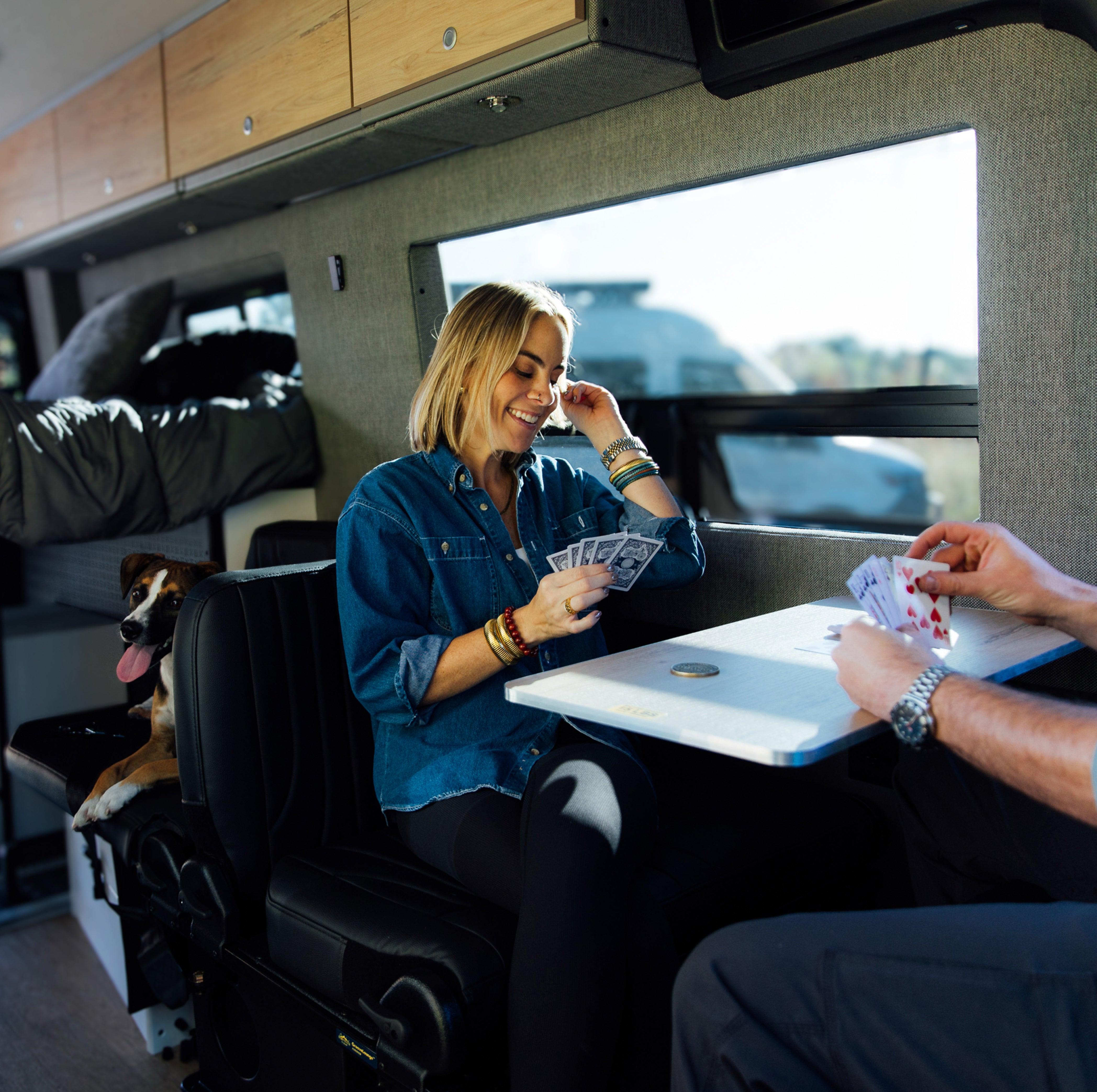 Couple playing cards with a dog inside a camper van, enjoying vanlife and adventure travel.