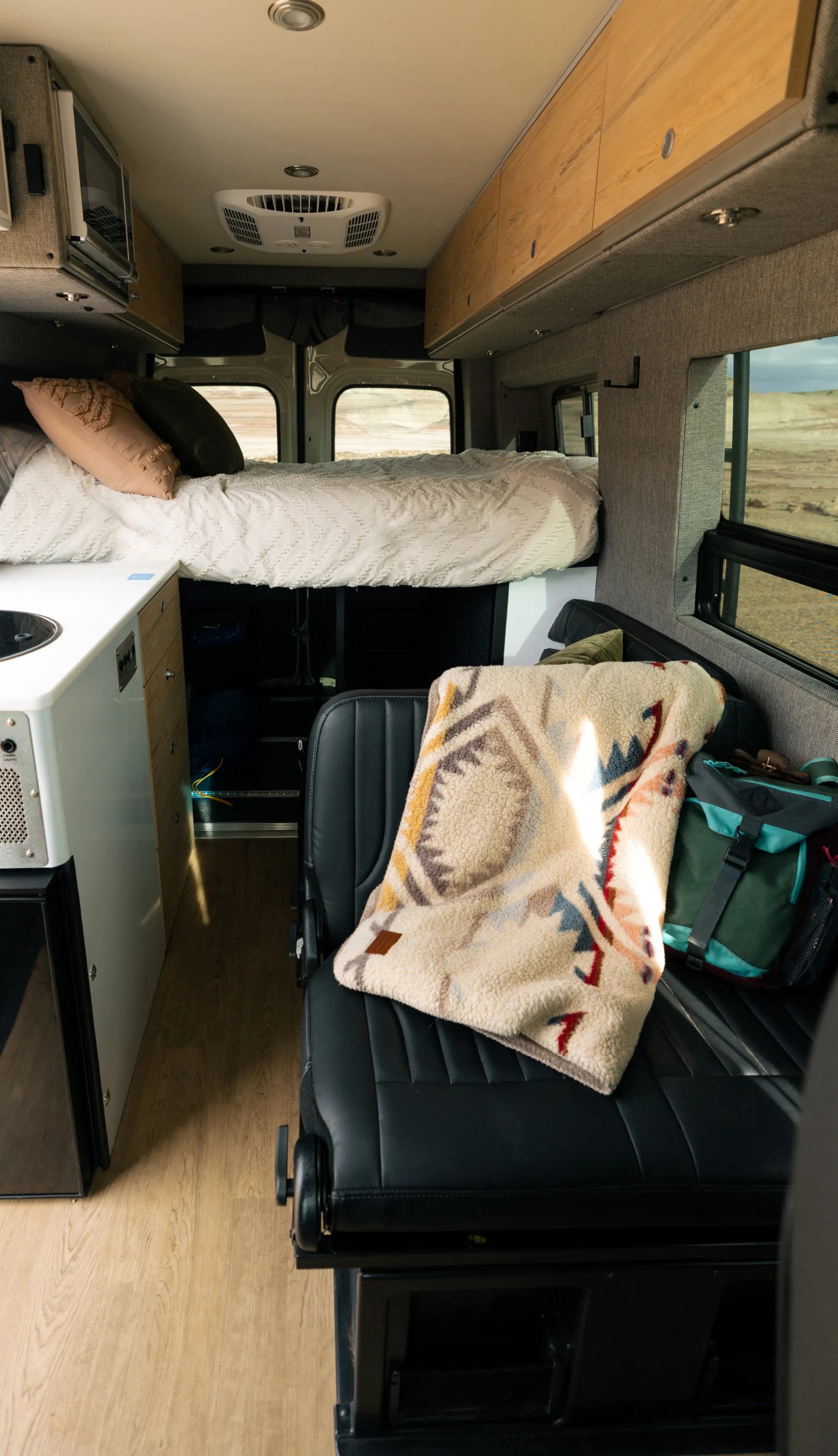 Interior of camper van with bed, storage cabinets, convertible seat, and cozy decor, ideal for vanlife, adventure van, or overlanding.