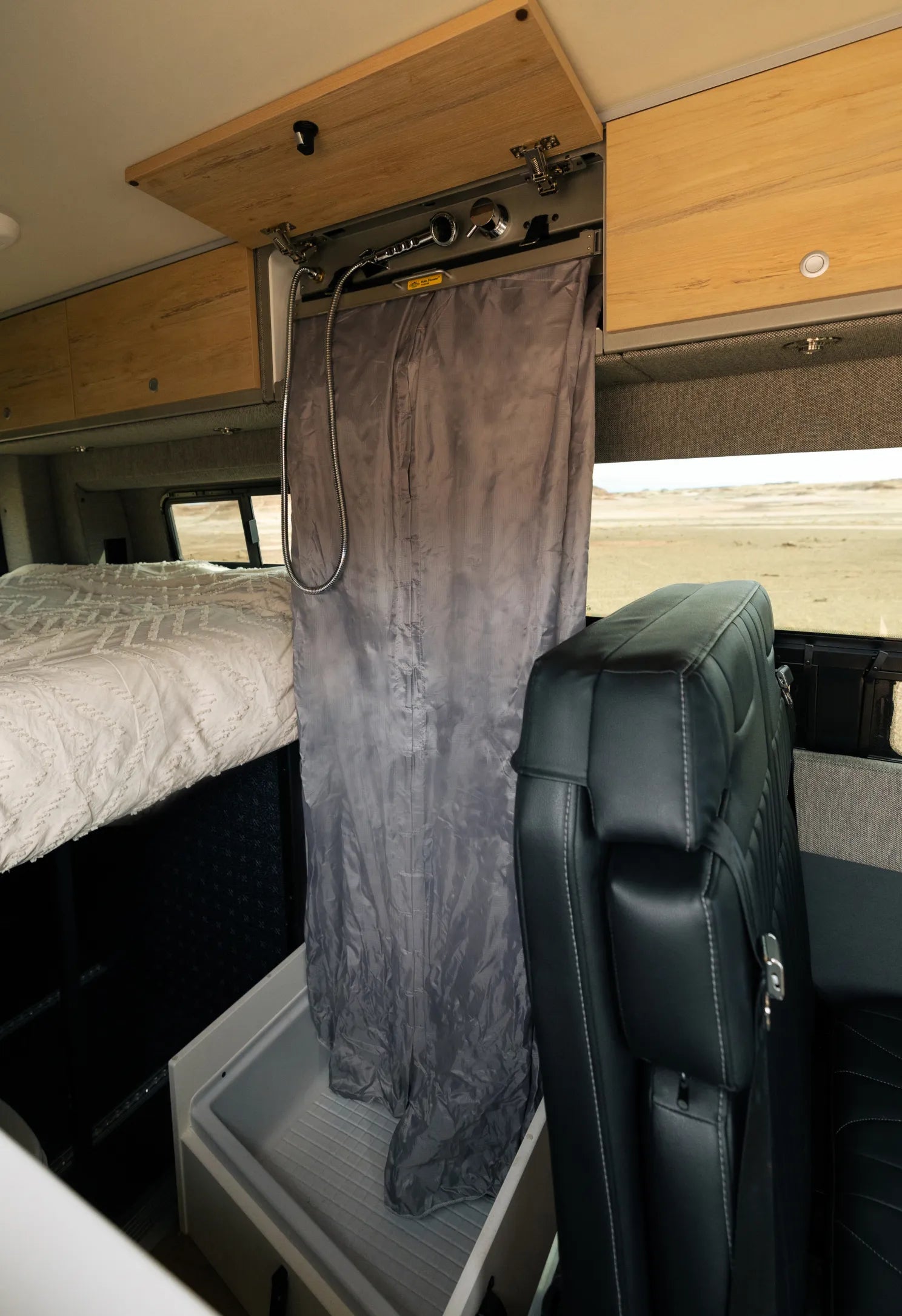 Camper van interior with convertible shower, bed, and black seat for vanlife and overlanding.