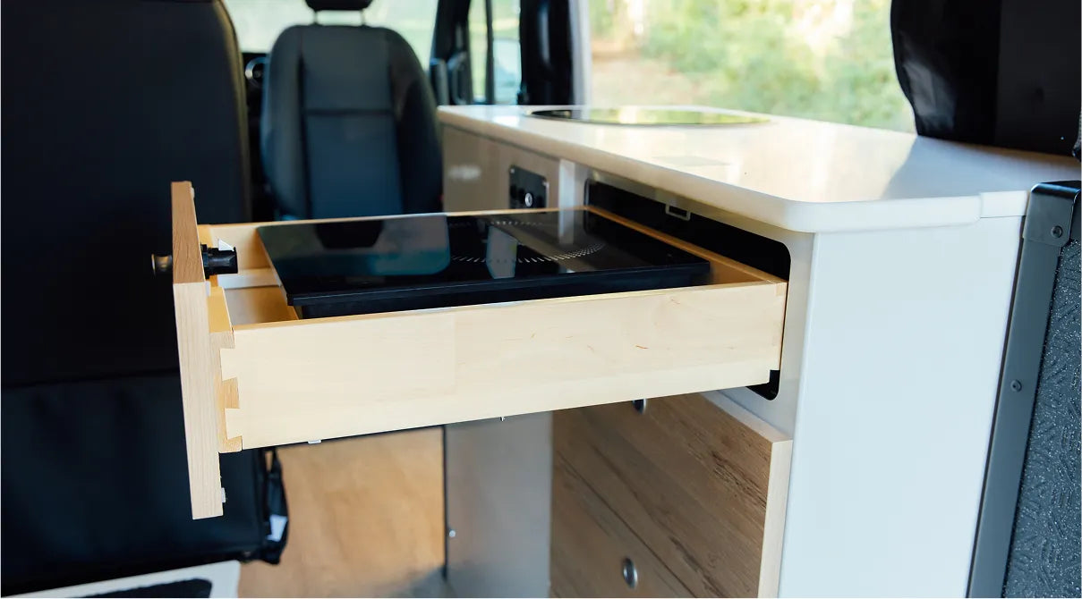 Camper van interior kitchen drawer open with induction cooktop, perfect for overlanding or vanlife.