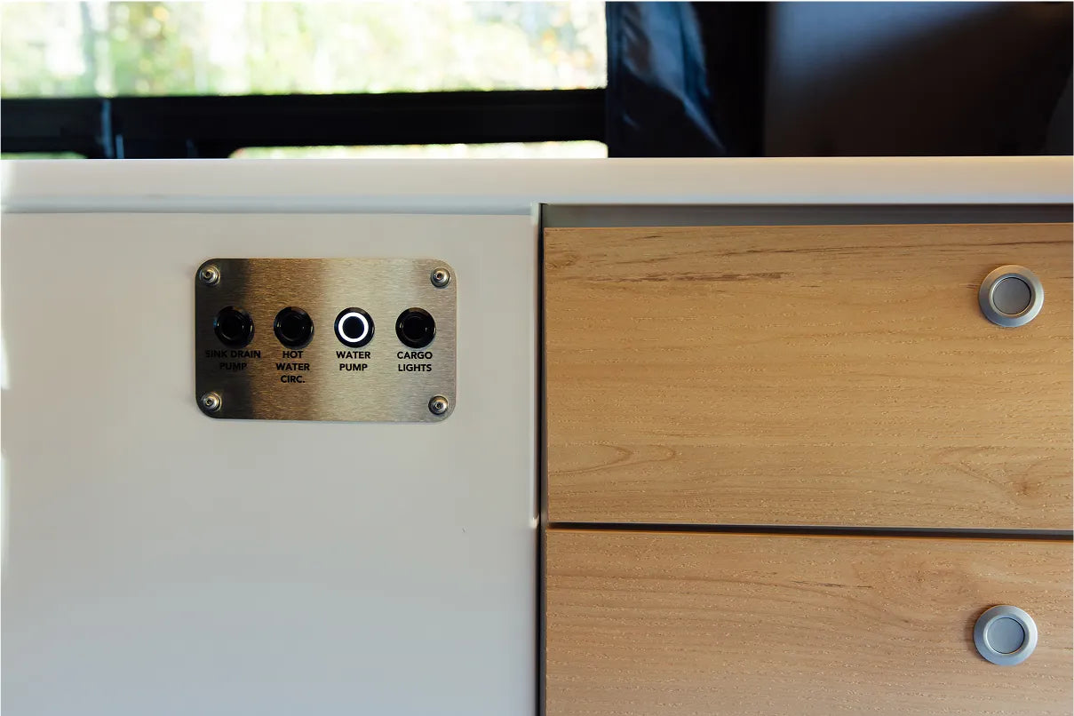 Camper van interior control panel for water pump and cargo lights beside wood drawers, ideal for vanlife, adventure van or Class B RV.