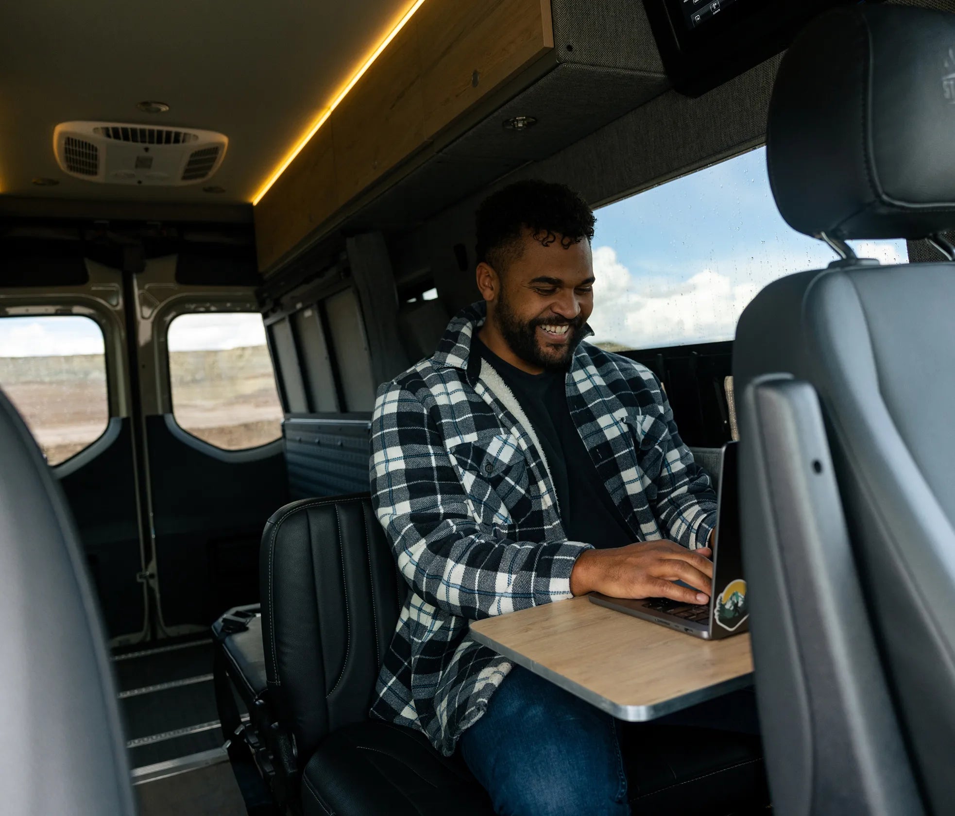 Interior of camper van with man working on laptop at table, showcasing vanlife adventure rig seating.