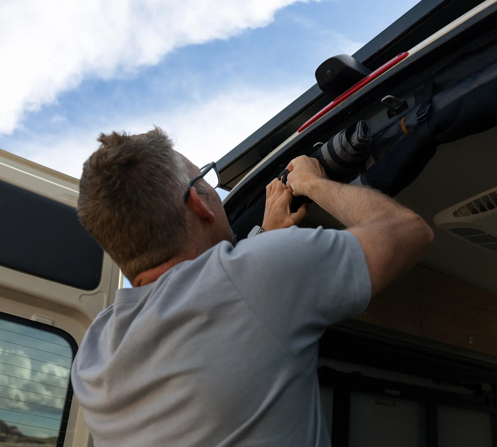 Person securing gear inside rear hatch of a Sprinter camper van, perfect for vanlife and overlanding.