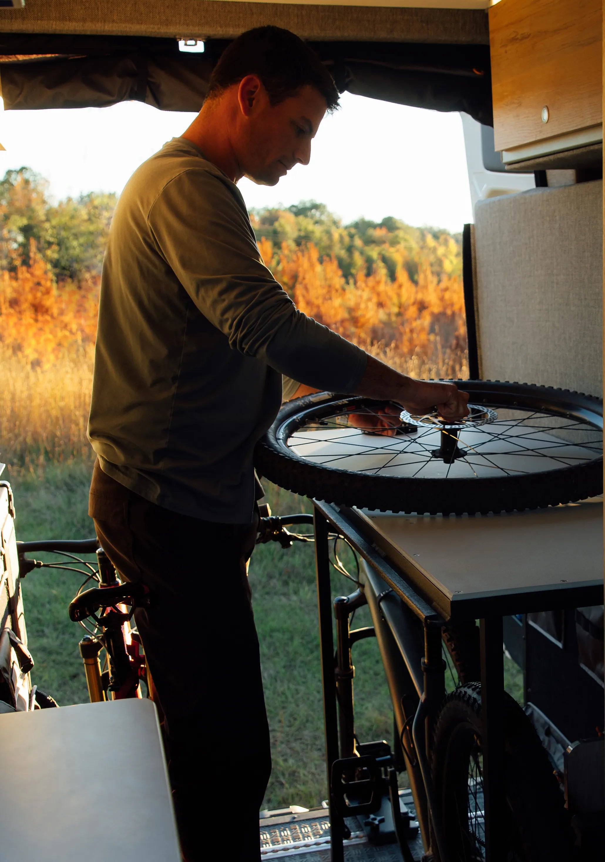 Person fixing mountain bike inside adventure van, camper van, overland road trip setting