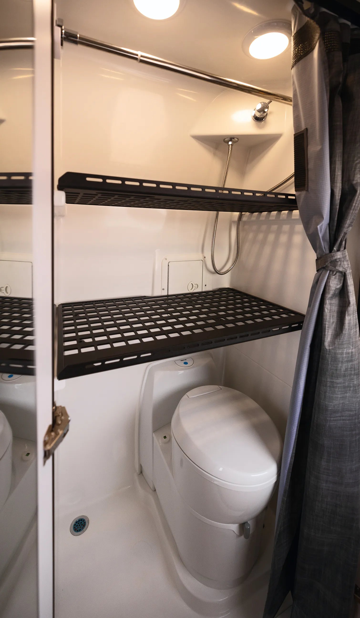 Modern camper van bathroom with toilet, shower, shelves, and curtain in adventure van.