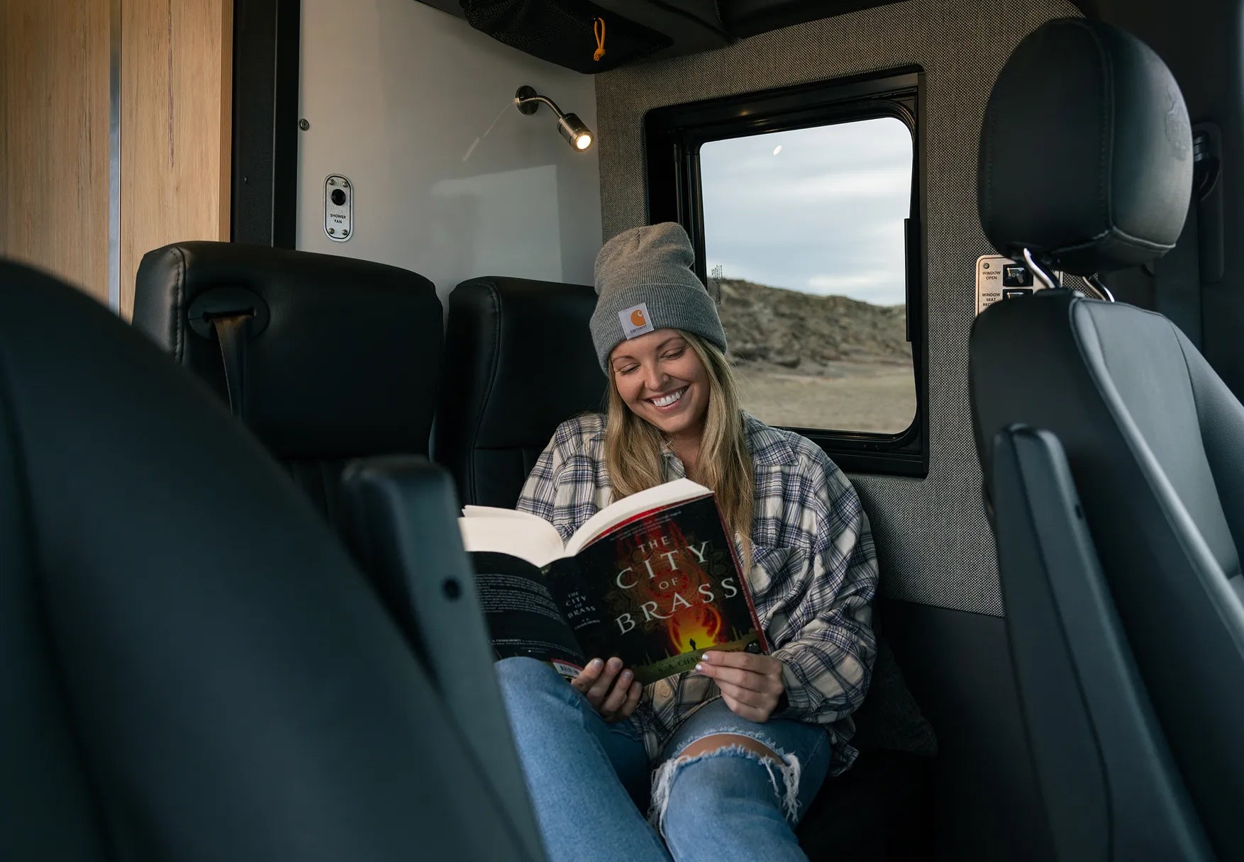Woman reading inside luxury camper van, showcasing adventure vanlife and nomadic lifestyle interior.