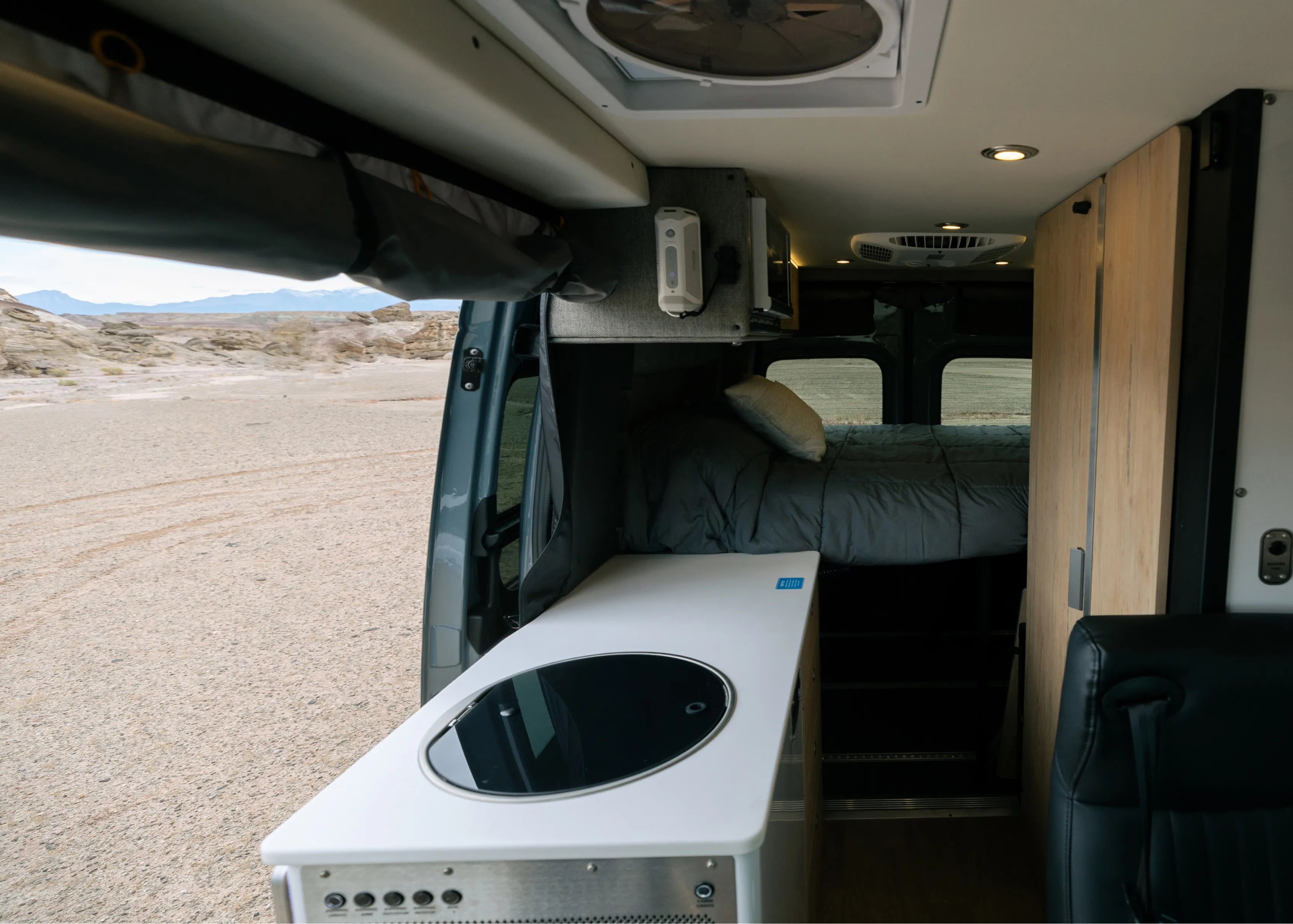 Modern adventure van interior with kitchenette, bed, and outdoor view, ideal for vanlife and overlanding.