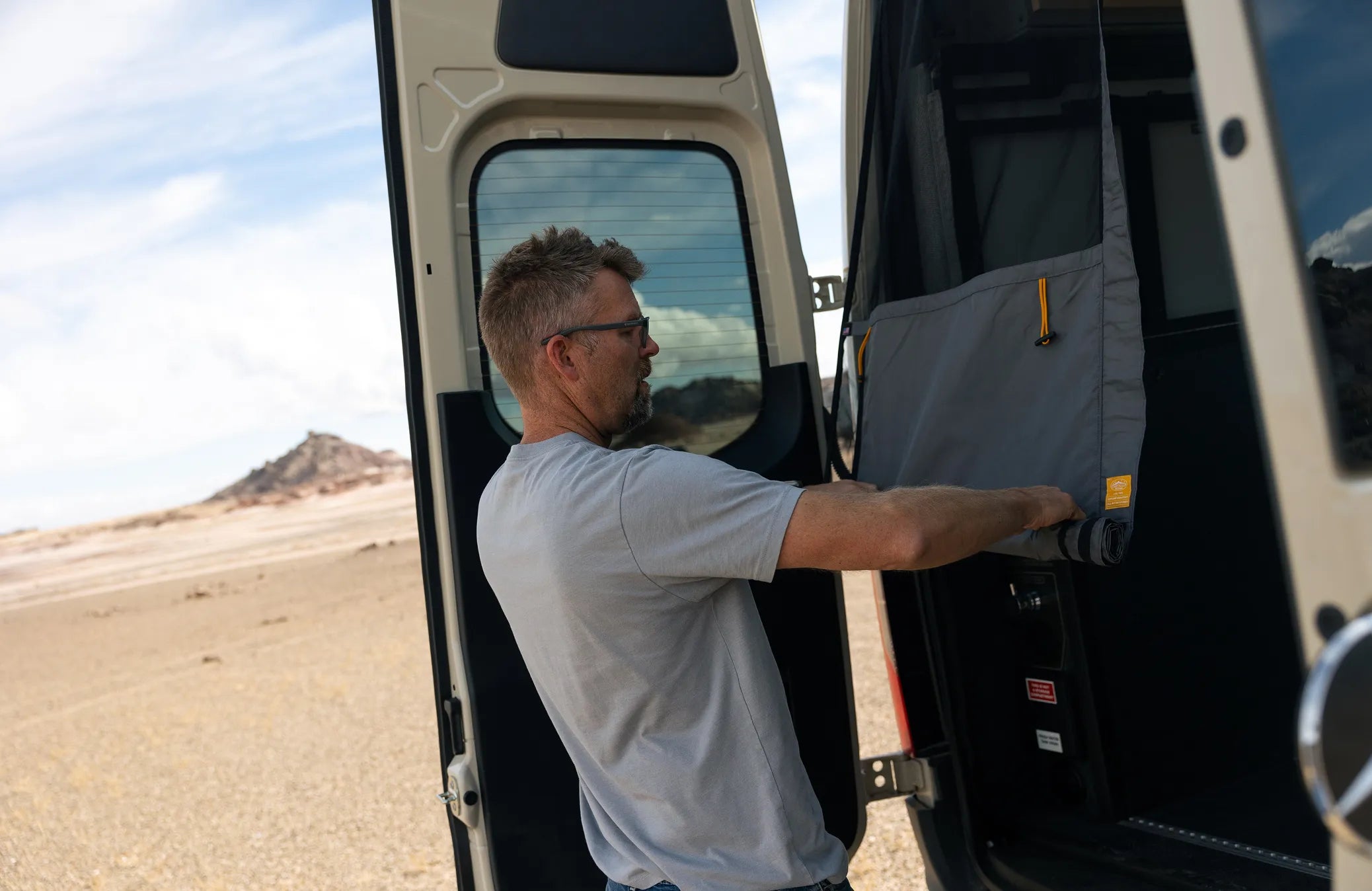 Man setting up storage in Sprinter camper van trunk, adventure vanlife desert road trip