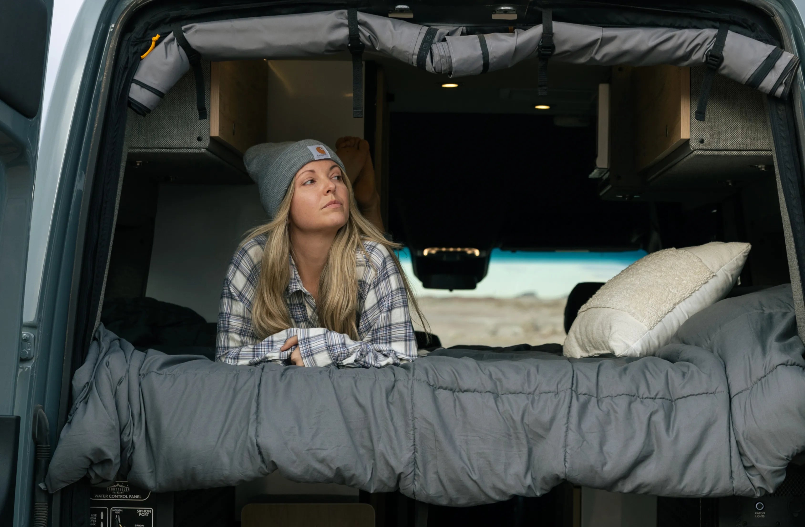 Woman relaxing on trunk bed inside an offroad camper van, embracing vanlife adventure.