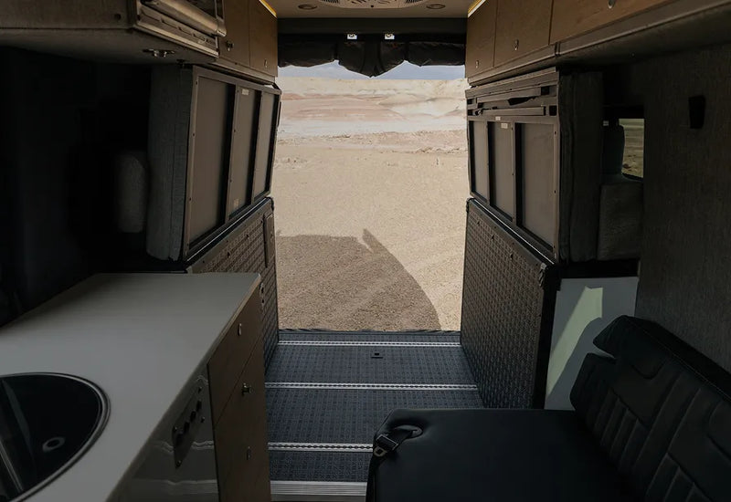 Flexible interior floorplan of adventure camper van with open rear doors and desert view, ideal for overlanding, vanlife, and road trips.