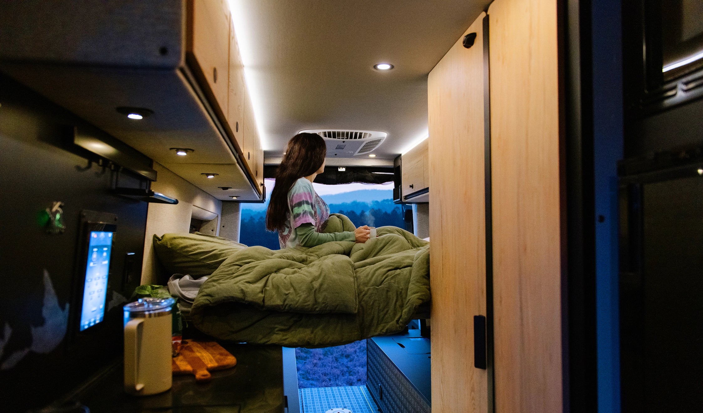 Woman relaxing in bed inside a modern camper van, enjoying vanlife and adventure travel.