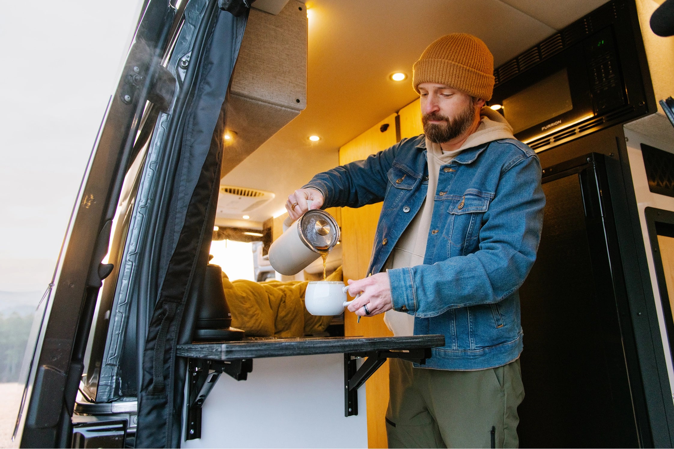 Man pours coffee in camper van kitchen, enjoying vanlife adventure travel in a Class B RV.