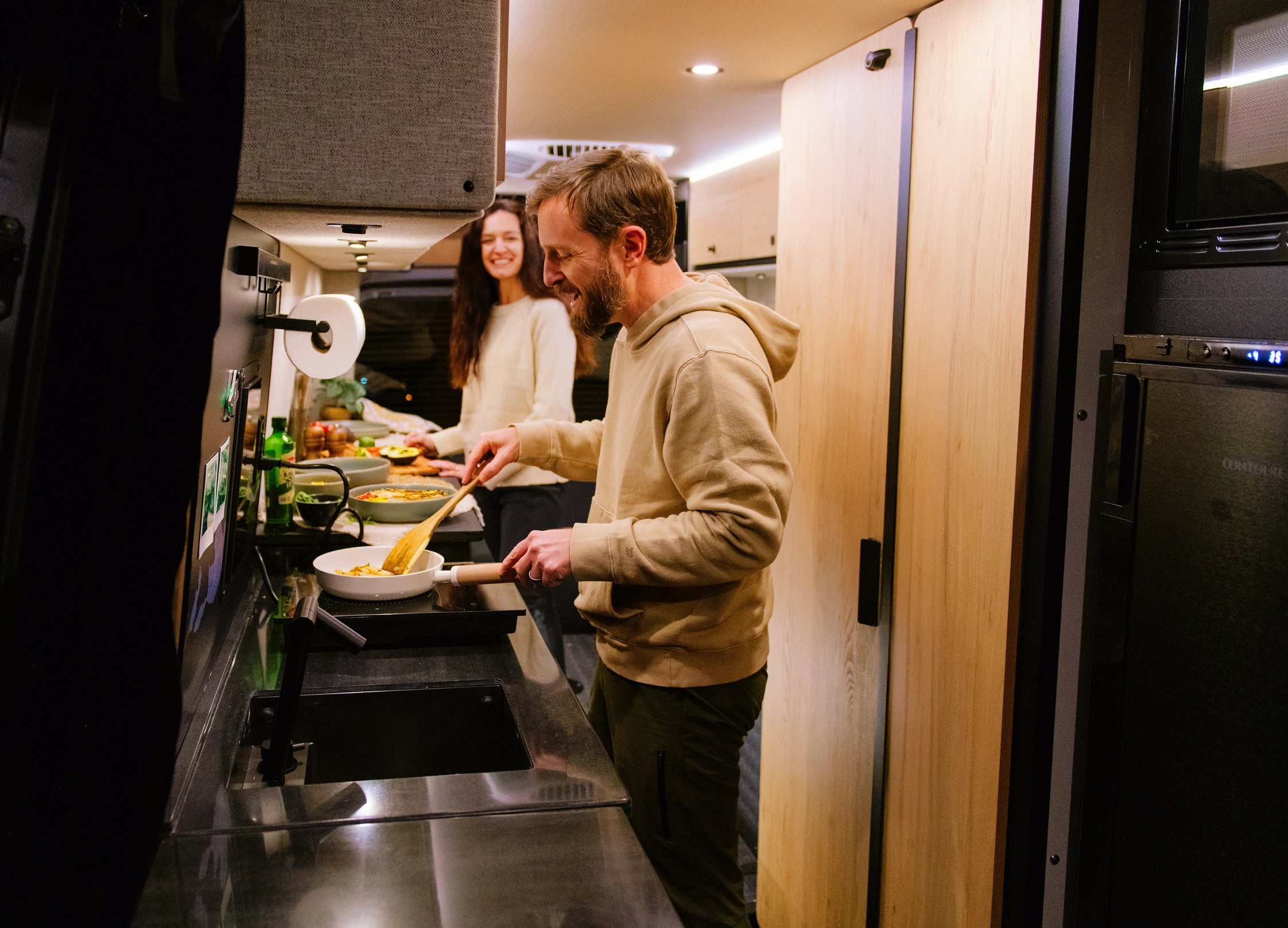 Couple cooking dinner in modern camper van kitchen, enjoying vanlife and adventure travel.