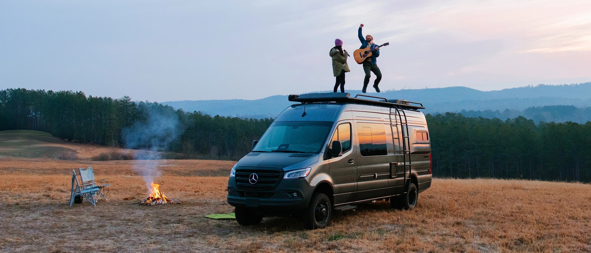 Sprinter 4x4 Camper Van parked in nature, people on roof, campfire, adventure van road trip