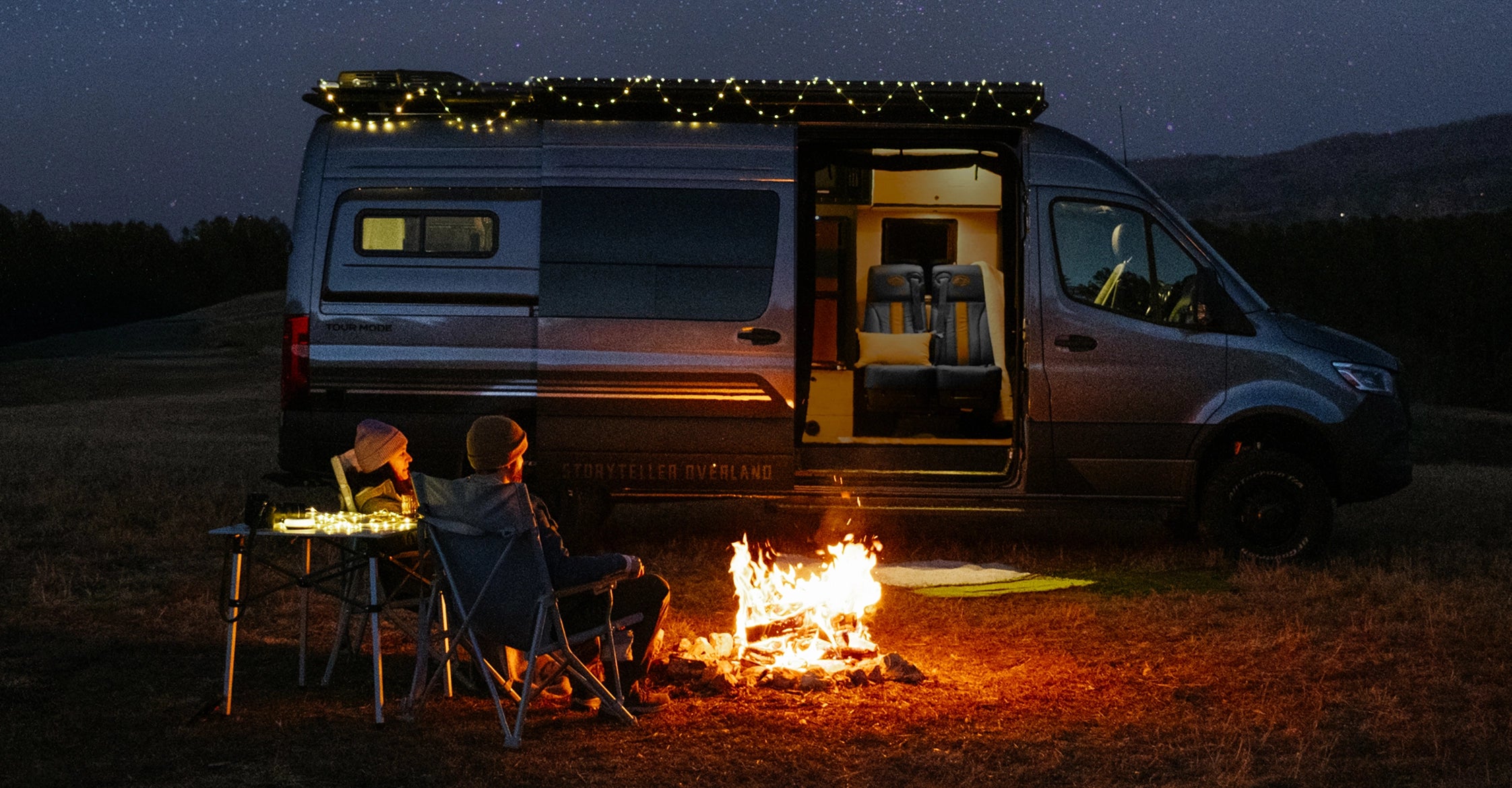 Adventure van with string lights, open doors, and campfire under starry sky, perfect for vanlife, overlanding, road trip, Class B RV, Sprinter 4x4 experience.