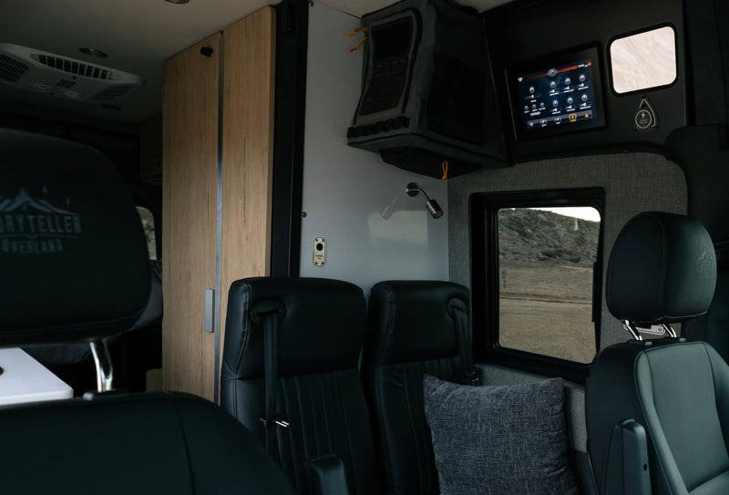 Modern interior of adventure van with black seats, control panel, and wood cabinetry, ideal for campervan or vanlife road trips.