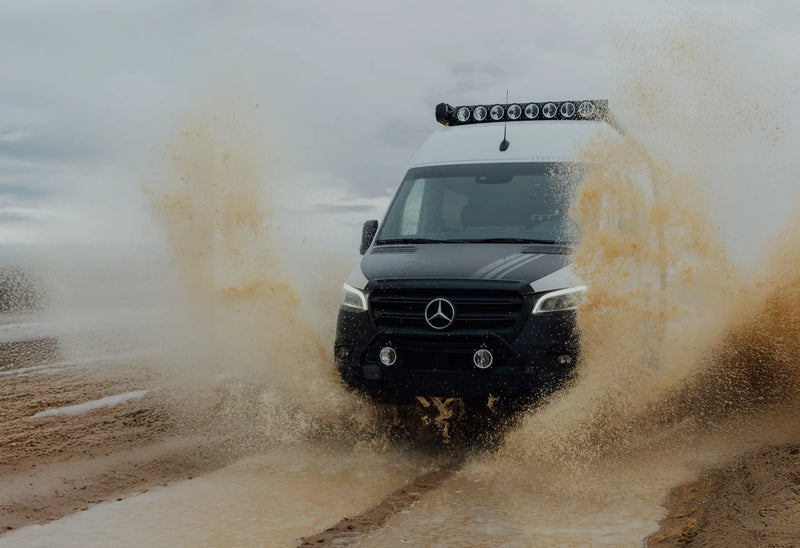 Sprinter 4x4 adventure van splashing through mud, ideal for overlanding and offroad vanlife.