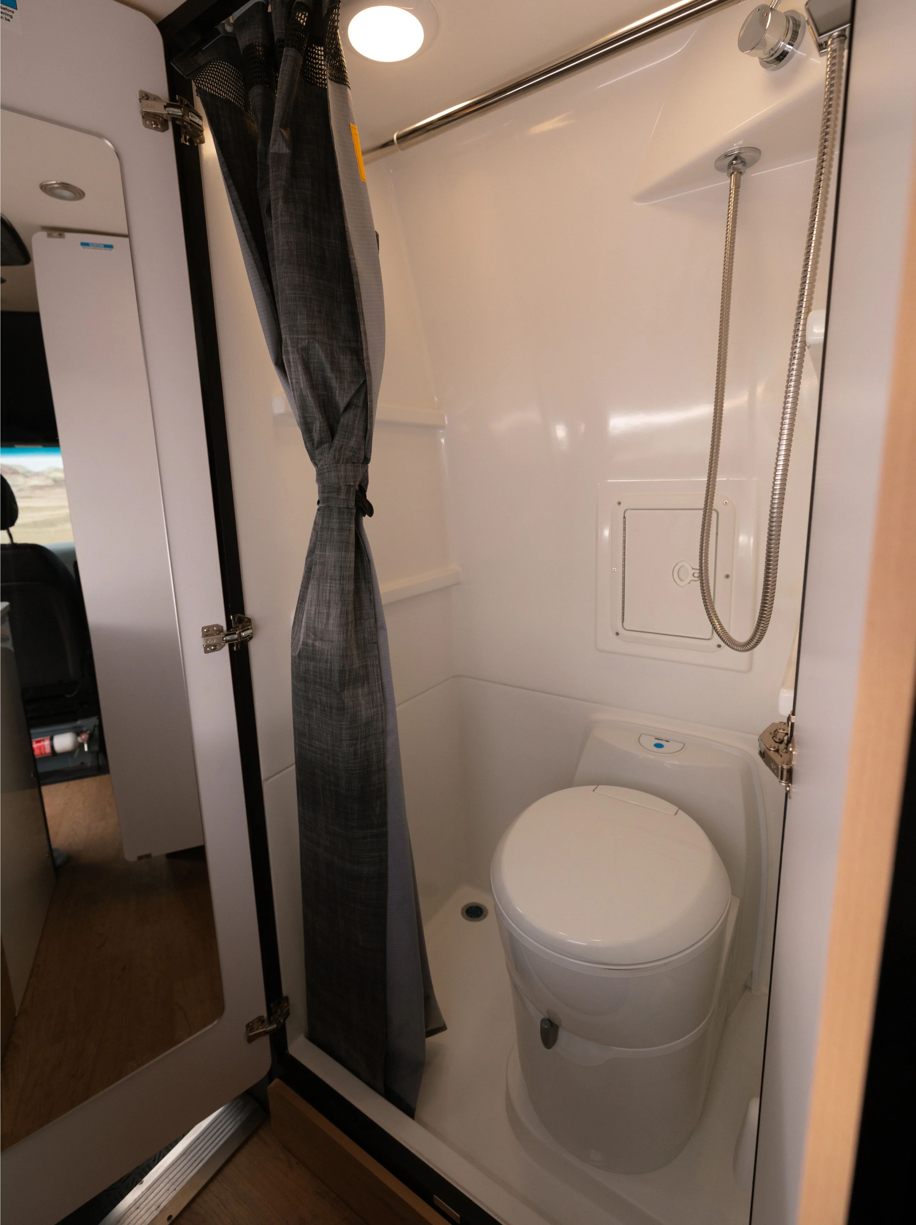 Compact wet bath with toilet, shower, and curtain inside a Class B camper van or adventure van.