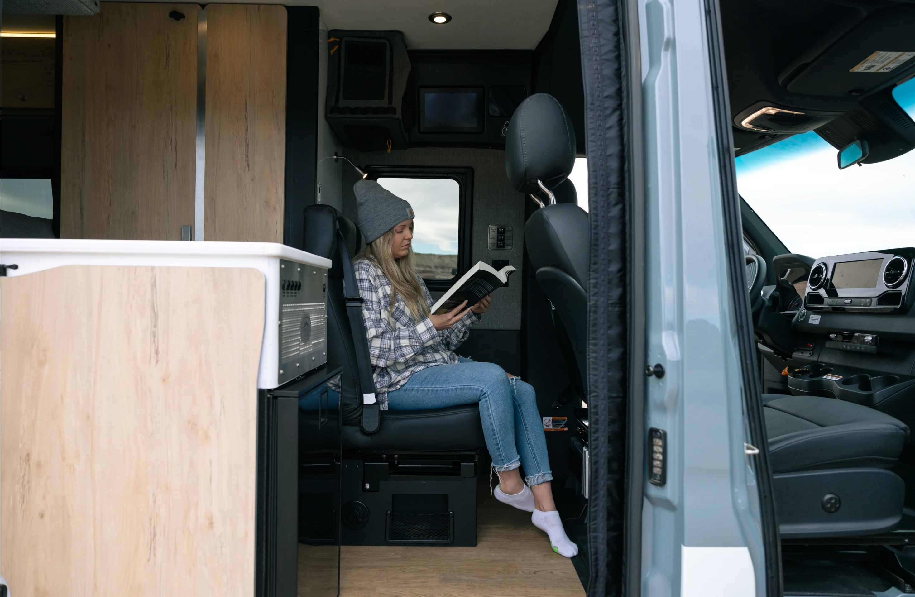 Woman relaxing and reading inside a Beast MODE adventure van campervan interior with wood cabinetry