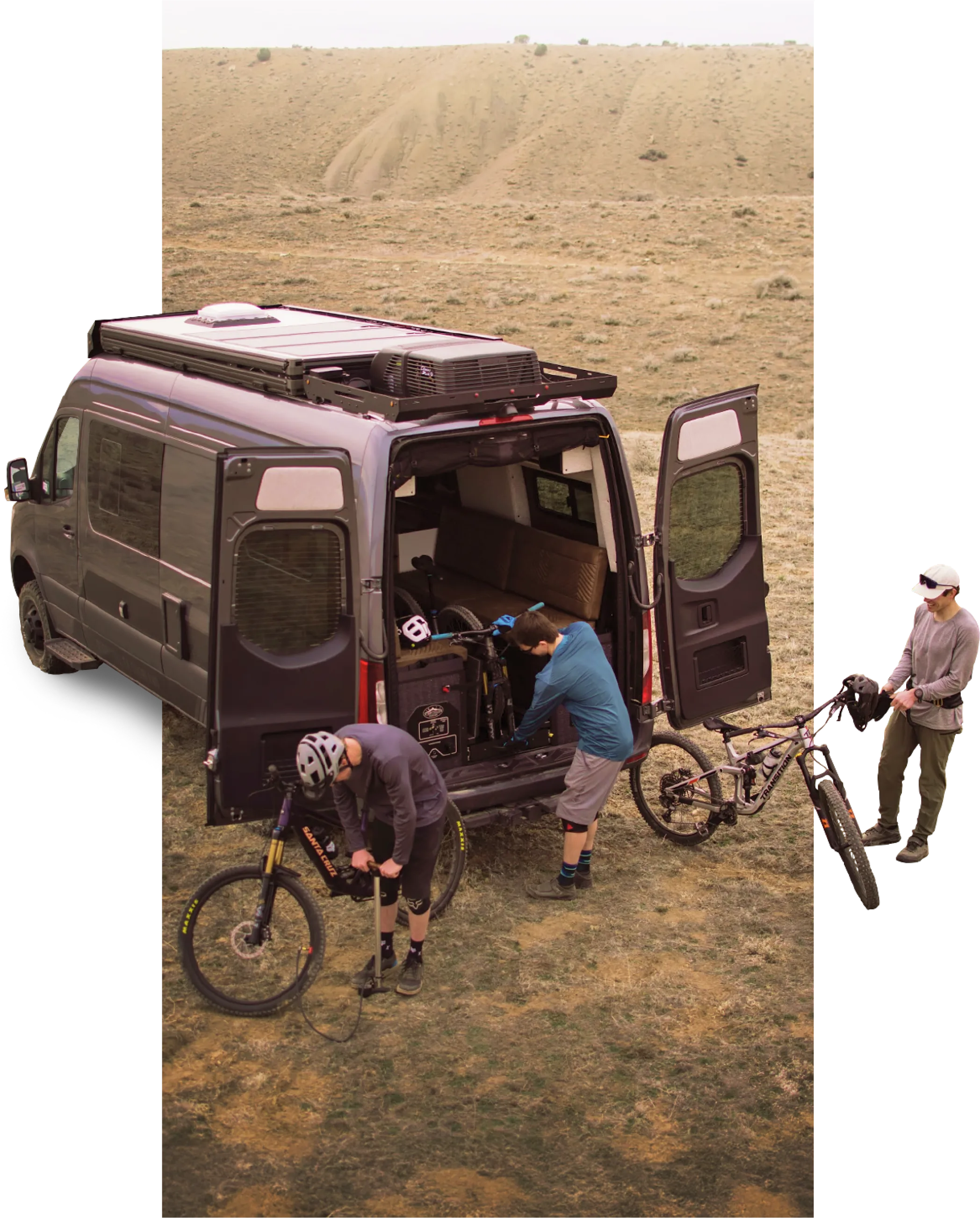Adventure van with open doors in rugged terrain, people preparing mountain bikes for vanlife road trip
