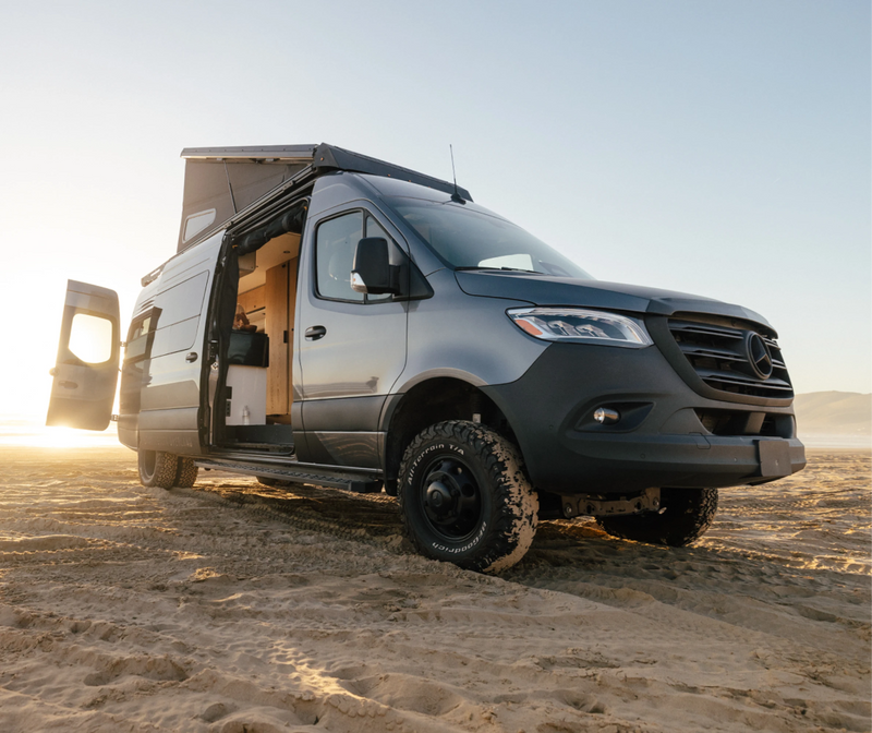 Sprinter 4x4 adventure camper van with pop-top roof on sandy beach at sunrise, ideal for overlanding and vanlife