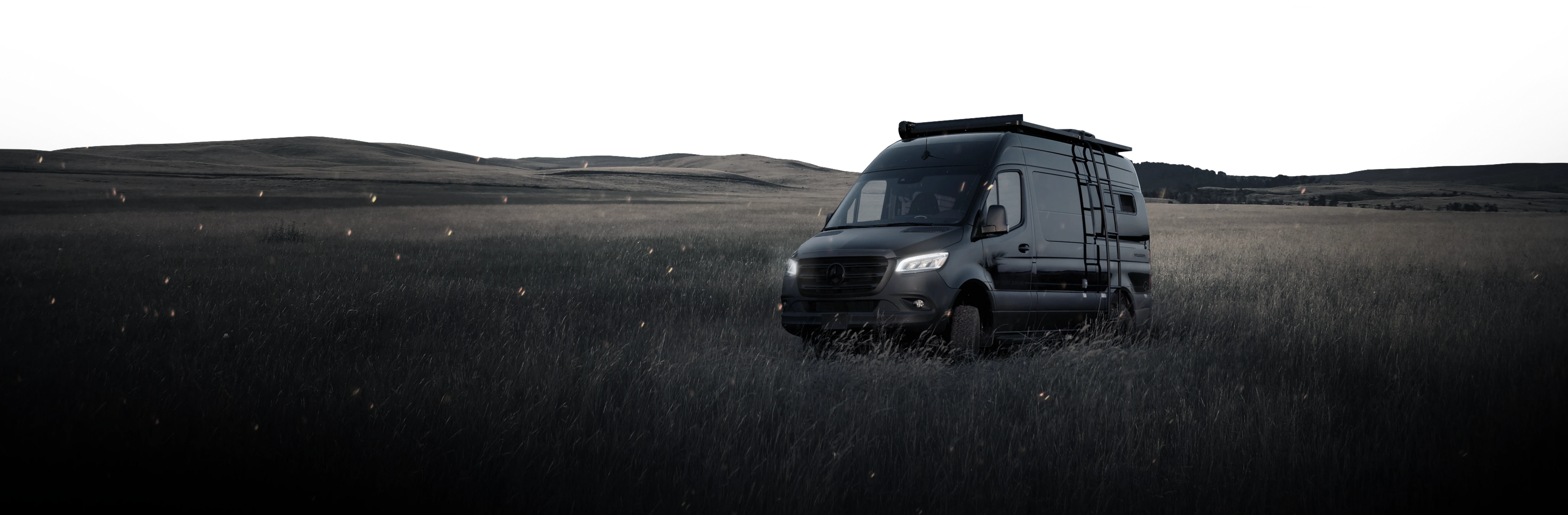 Black Sprinter 4x4 camper van for overlanding and vanlife parked on grassy field at dusk