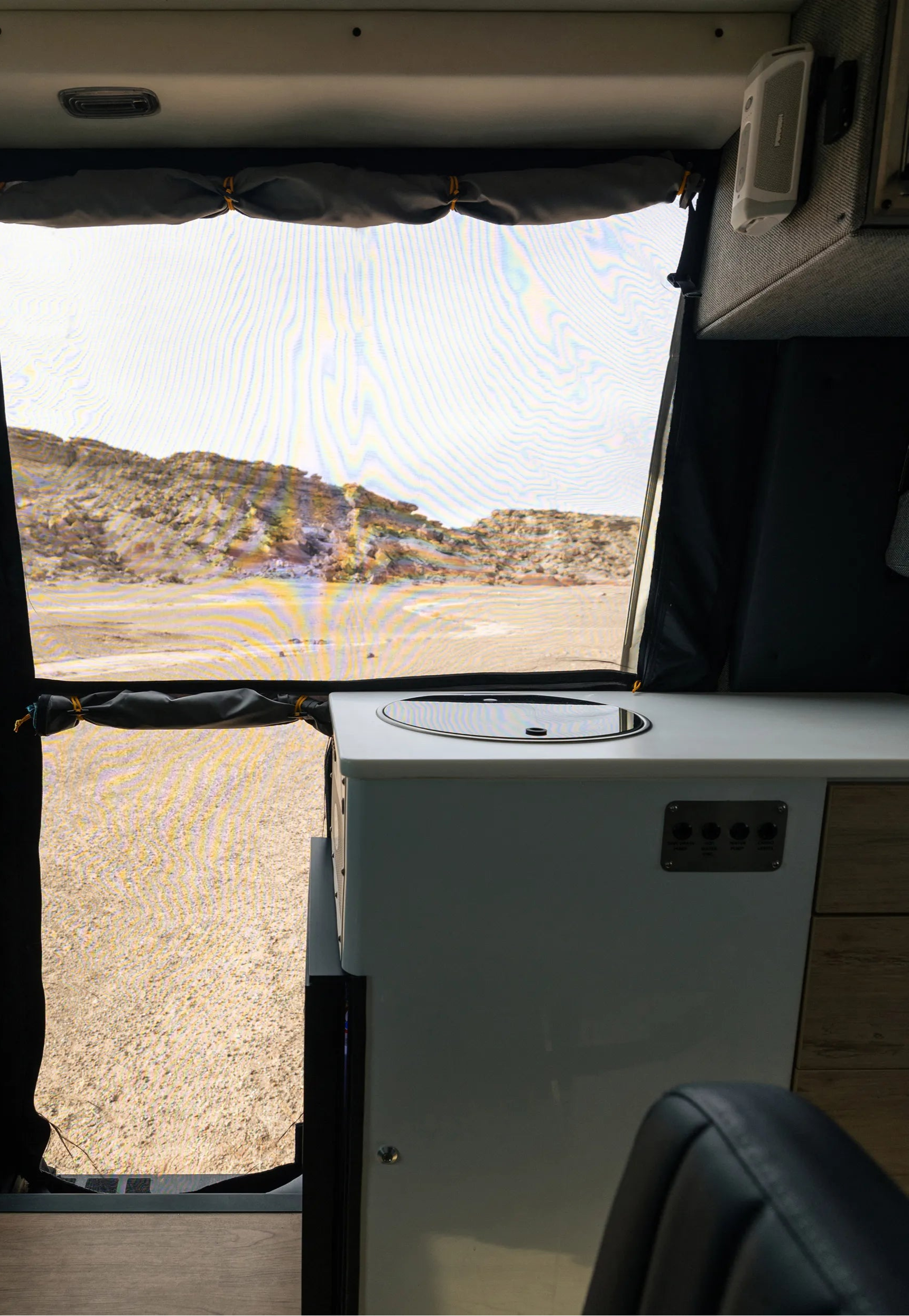 Camper van interior with compact kitchen, screen door, and desert landscape view for overlanding